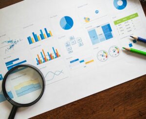 Top view of business analytics paper including charts and notes with a magnifying glass and pencils.